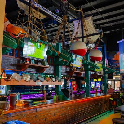 A lively bar with a nautical theme features sails and ropes, TVs, and vibrant lighting.
