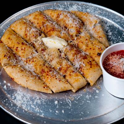 Garlic bread slices with grated cheese and marinara sauce on a metal tray.