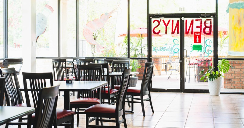 Interior of a restaurant with black chairs, tables, large windows and a glass door.
