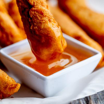 Chicken finger dipped in a sauce on a plate of chicken fingers, close up.