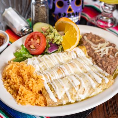 Enchiladas in green sauce drizzled with crema, served with rice, beans, and fresh salad.
