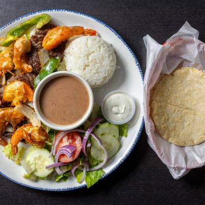 Steak and shrimp with salad, beans, rice, and tortillas.