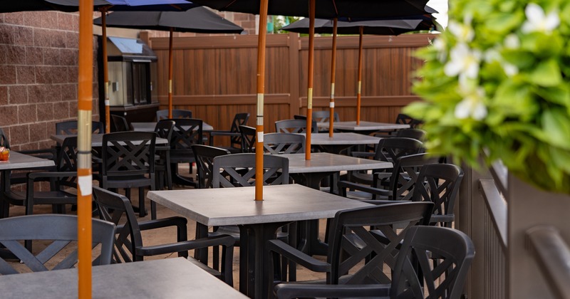 An outdoor patio area with dark wooden tables, chairs, and large umbrellas