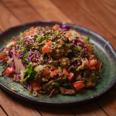 Thai Steak Salad with diced tomato, scallions, purple cabbage, and sesame seeds.