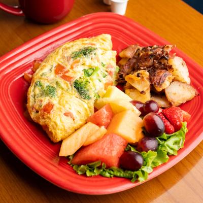 Vegetable omelet served with home fries and fruit fruit.
