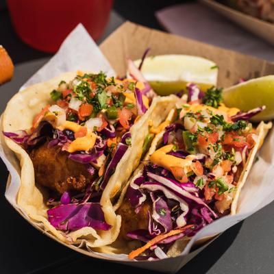 Baja Fish Tacos topped with sauce and pico de gallo, served with lime wedges.