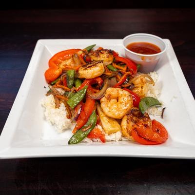 Stir-fried shrimp and vegetables served over white rice with a cup of red sauce.