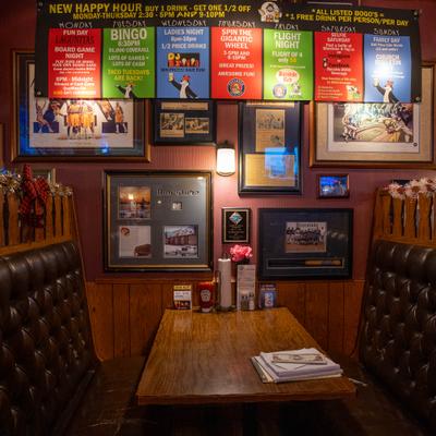 A leather booth with wooden table, wall adorned with framed pictures and event posters.