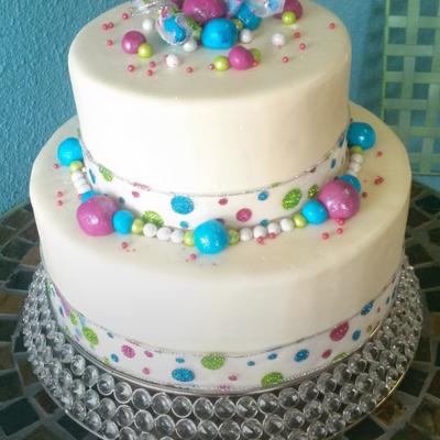 A two-tiered white cake decorated with multi colored shimmering balls.