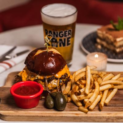 Double cheeseburger on a pretzel bun with fries, ketchup, and a glass of beer.