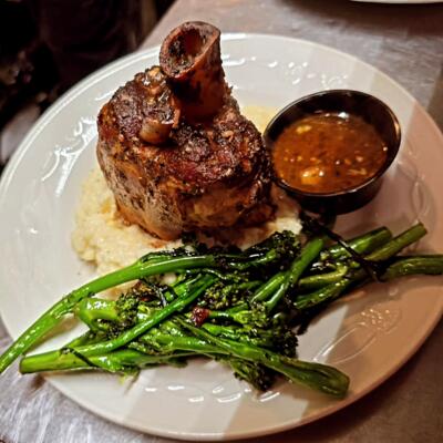 Lamb shank served over mashed potatoes with broccolini and a side of sauce.