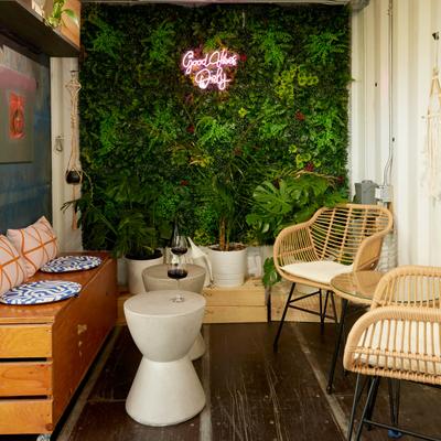 Interior with wicker furniture and a neon Good Vibes Only sign on a greenery wall.