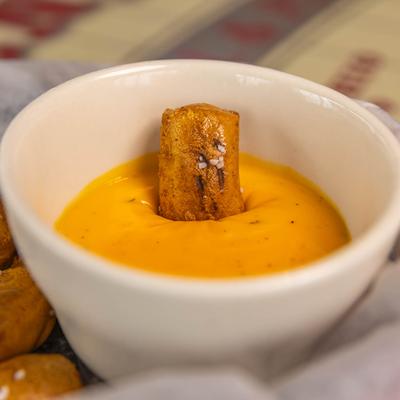 A pretzel bite dipped in a bowl of beer cheese dip.