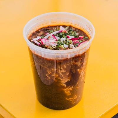 Mexican ramen served in a plastic cup, garnished with diced onion and cilantro.