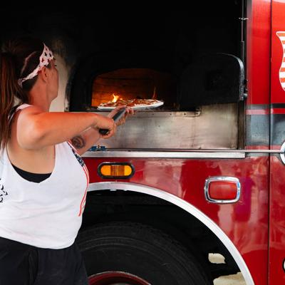 A food truck worker placing an uncooked pizza inside the oven using a peel.