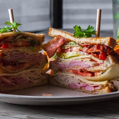 Stacked club sandwich with lettuce, tomato, ham, cheese, and bacon.