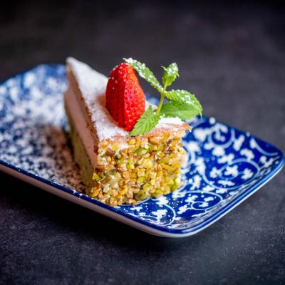 A slice of pistachio dessert topped with a strawberry and mint.