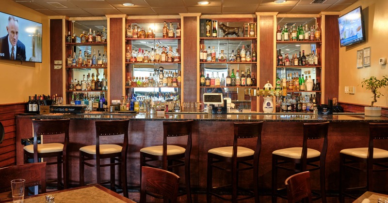 A bar with bar stools and bottles on the shelves
