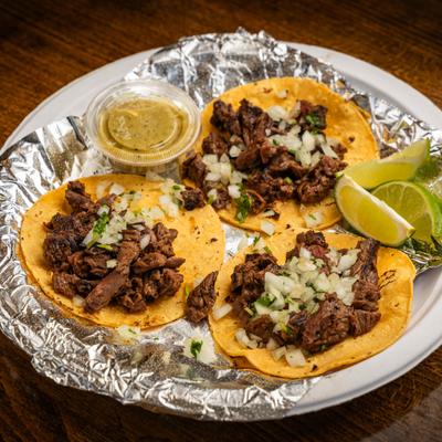 Street tacos topped with onions and cilantro, served with lime and green salsa.