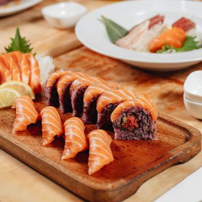 Salmon Sashimi served with salmon maki rolls on a wooden board.