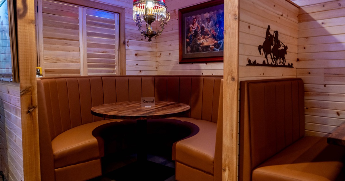 Rustic restaurant booth with a round wooden table, tan leather seating, and a red chandelier