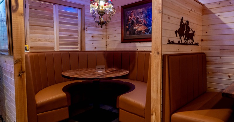 Rustic restaurant booth with a round wooden table, tan leather seating, and a red chandelier