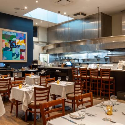 Open kitchen restaurant with bar seating, set dining tables, and wall art.