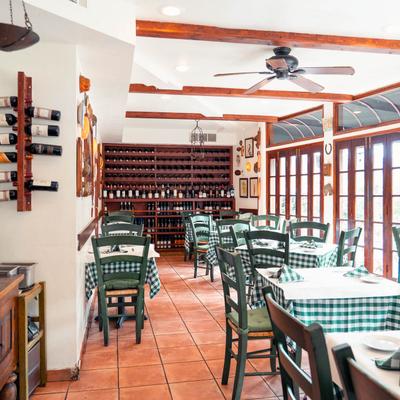 Interior featuring green-and-white checkered tablecloths, wooden wine racks, and large windows.