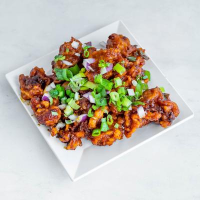 Fried golden cauliflower flowerets, with tomato and garlic sauce, red onion, and scallions.