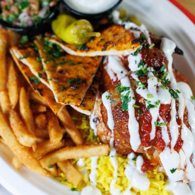 Rotisserie Chicken with rice, fries, pita, white, creamy sauce, and a small chopped salad.