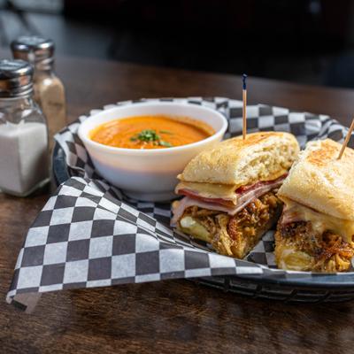 Cubano Sandwich cut in half and served with bowl of topmato soup.