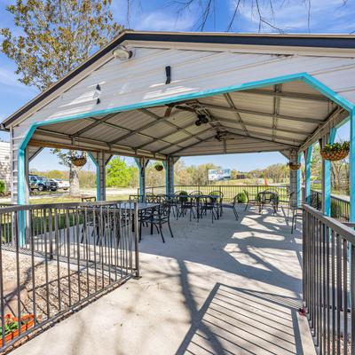 A covered outdoor seating area, featuring tables, chairs, and hanging plants.