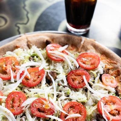Pizza topped with lettuce, tomato, and onions.