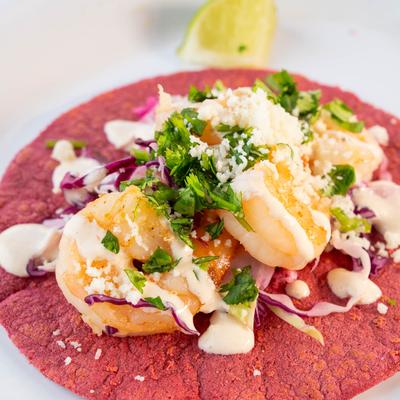 Shrimp taco served on a red tortilla.