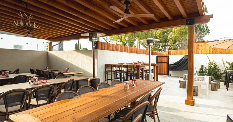 Open-air dining area with wooden tables, chairs, patio heaters, ceiling fan