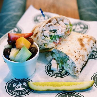 Chicken Ranch wrap served with a small bowl of fresh fruit and a pickle spear.