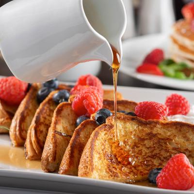 French toast with fresh berries, being drizzled with maple syrup.