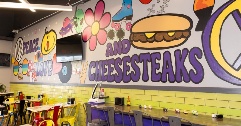 Interior with a colorful mural reading "Peace Love and Cheesesteaks" with cartoon illustrations.