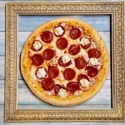 Pepperoni pizza presented within a gold picture frame against a wooden background.