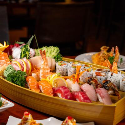 A large assortment of sushi and sashimi served in a traditional wooden boat shaped tray.