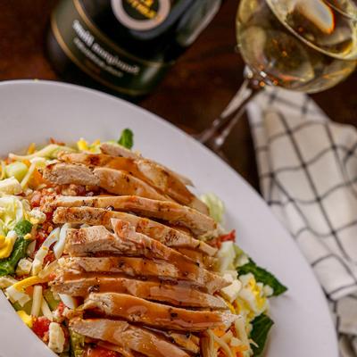 Grilled chicken on veggies and cheese, served with a glass of white wine