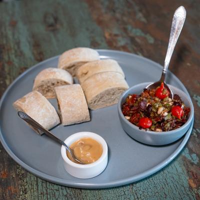 Mediterranean-style olive tapenade alongside sliced baguette and another dip.