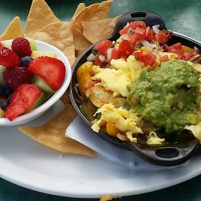 Burrito bowl with guacamole, cheese, tomatoes, onion and a bowl of fruits