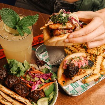 Hand holding a bao bun next to fries, salad, and drink.