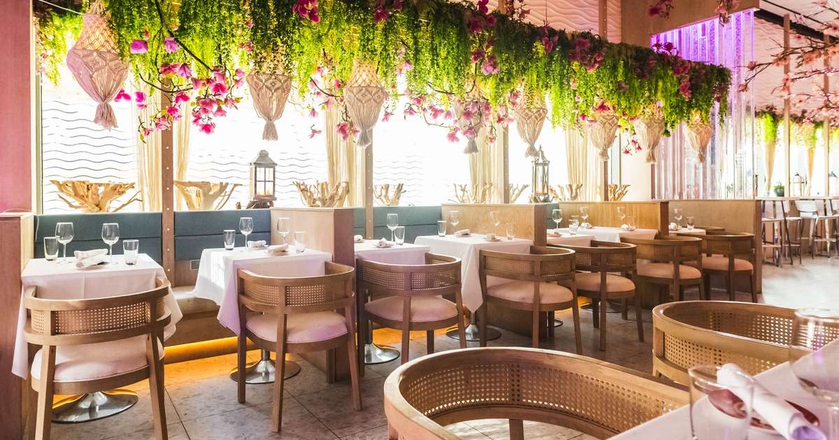 Interior seating area with tables set with white tablecloths and hanging greenery