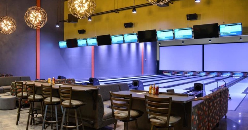 Modern bowling alley with multiple lanes, overhead scoring monitors, and bar seating