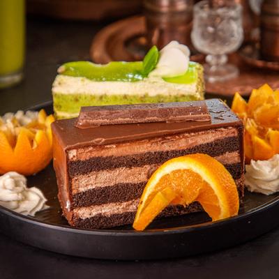 A plate with chocolate cake and pistachio cake slices, garnished with orange slices.