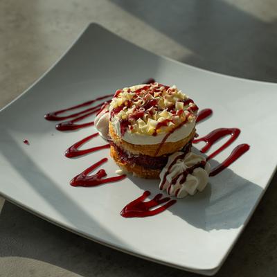 A mini layered sponge cake with cream, red jam, and white chocolate shavings.