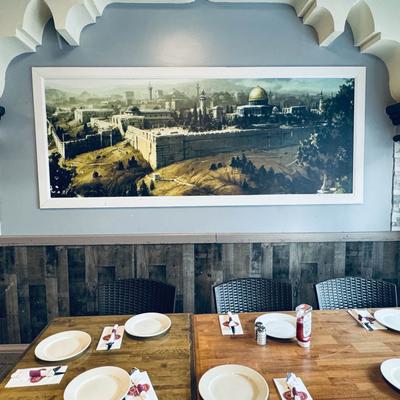 Interior, a large framed print of Jerusalem on the wall, and tables set with plates and cutlery.