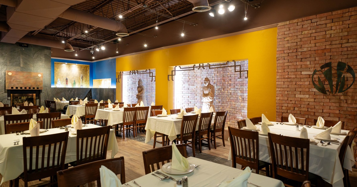 An elegant restaurant dining area with white tablecloths, wooden chairs, and exposed brick walls
